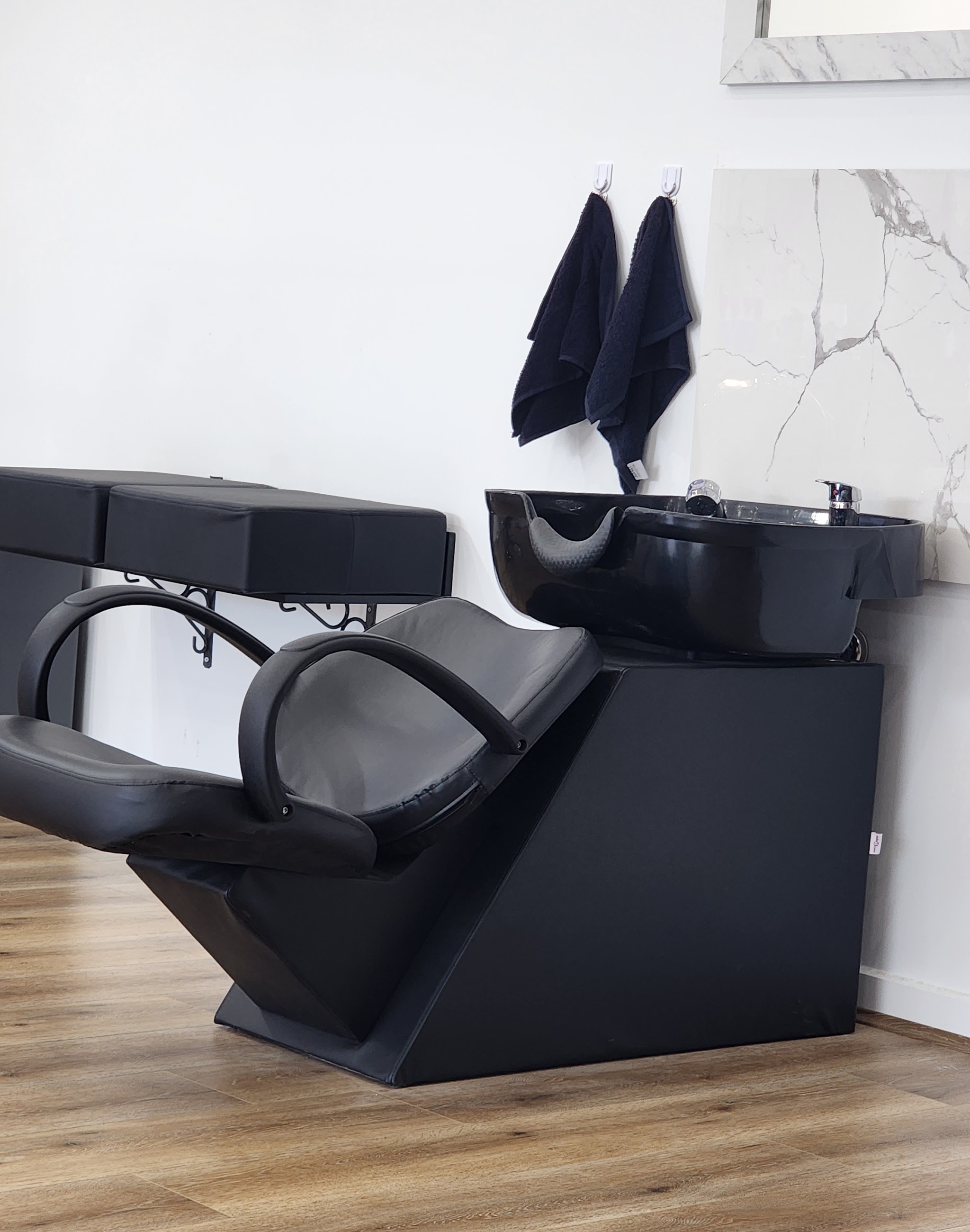 Black wash basin and reclining chair with towels and a marble splashback