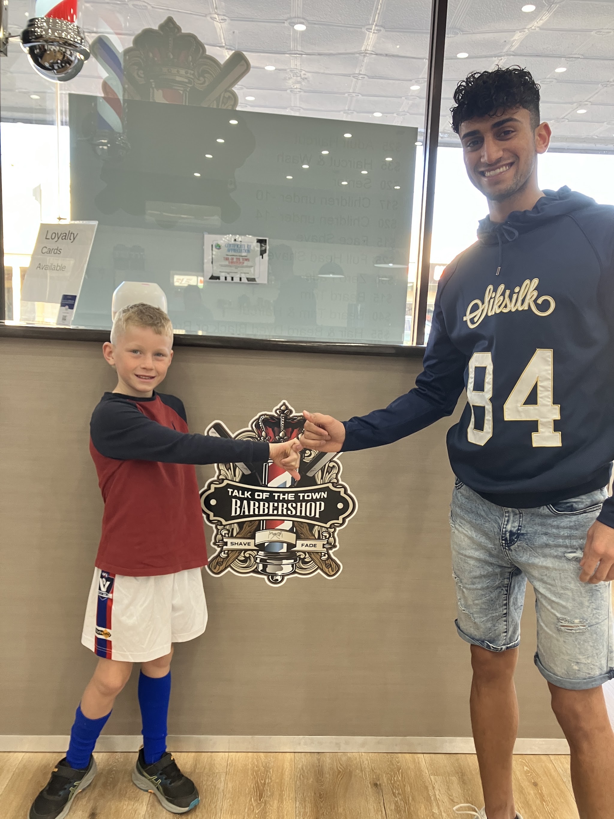 A barber fist-bumping a young customer in front of the Talk of the Town Barbershop wall decal