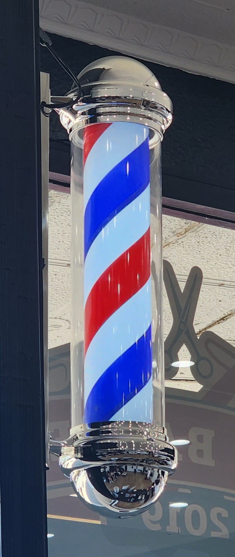 The illuminated red, white and blue barber pole at the shop